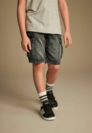 Shorts cargo in denim nero con molte tasche, abbinati a sneaker nere e calzini bianchi a righe. T-shirt grigia a girocollo parzialmente visibile.