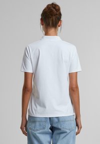 Hvit polo skjorte med korte ermer, klassisk krage og avslappet passform. Båret med lyseblå denimjeans, enkle uten synlige mønstre.