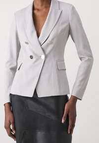 Blazer doppiopetto grigio chiaro con rever a punte, bottoni metallici, tasche laterali e una vestibilità su misura. Tessuto testurizzato.