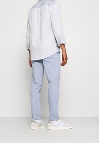 Camicetta azzurro chiaro con maniche arrotolate, abbinata a pantaloni slim-fit azzurro chiaro e sneakers grigie e bianche. Design semplice e informale.