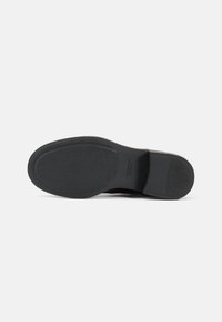 Black rubber sole with textured surface, rounded heel, and circular grip patterns. Minimalist design with embossed brand logo detail.