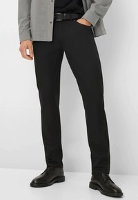 Zwarte rechte broek van gladde stof, met voorzakken en riemlussen, gestyled met een bijpassende zwarte leren riem en schoenen.