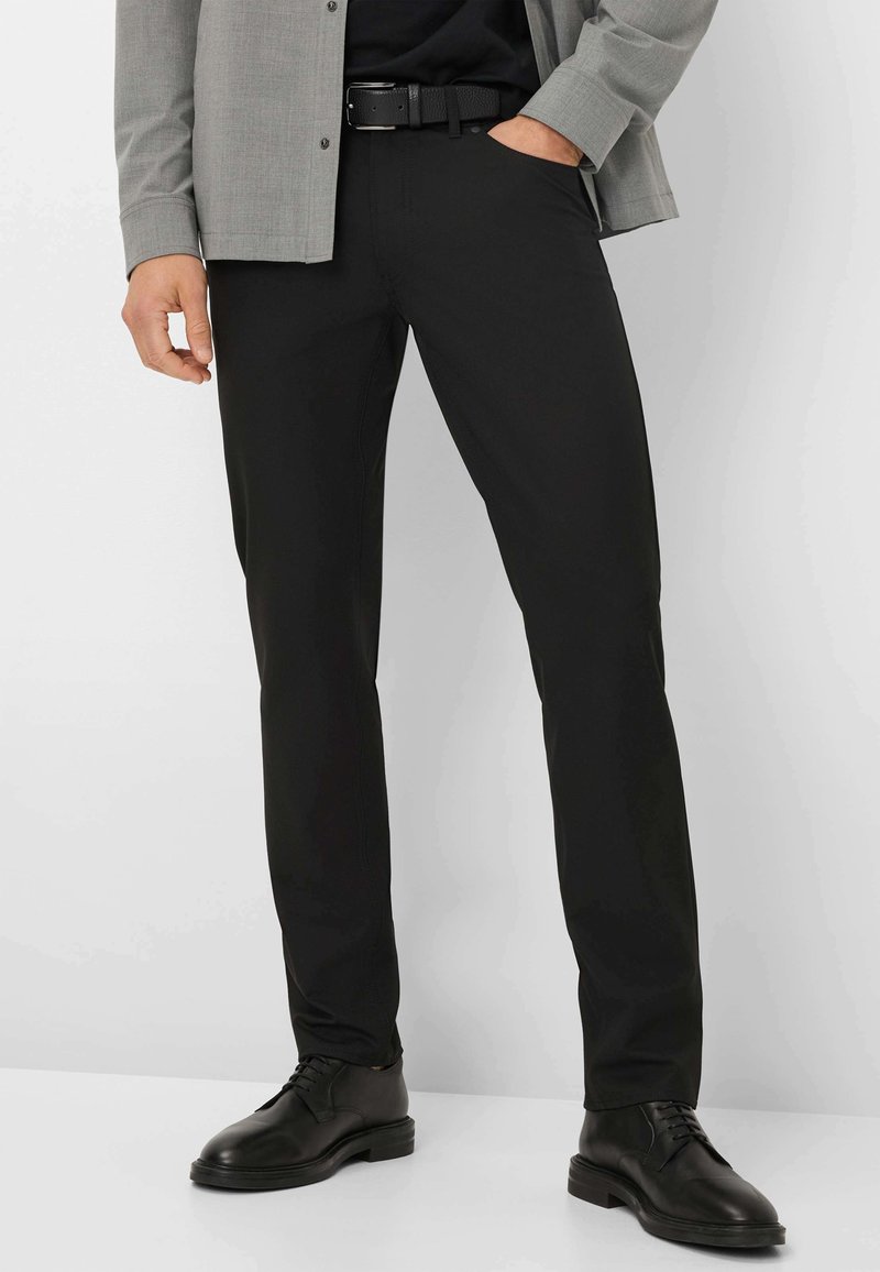 Zwarte rechte broek van gladde stof, met voorzakken en riemlussen, gestyled met een bijpassende zwarte leren riem en schoenen.