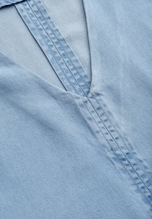 Hellblauer Stoff mit sichtbarer Naht und mehreren parallelen Nählinien, die ein V-förmiges Muster bilden.