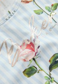 Tissu rayé bleu clair et blanc avec une rose rose et un texte argenté indiquant "Baker by Ted Baker."