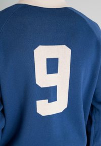 Blue sports jersey with white number 9 on the back, worn by a person, showing fabric texture and shoulder seam details.