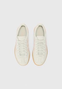 Buty sportowe z górą ze skóry zamszowej w jasnym kremowym kolorze, miękkim różowym wzorem z trzema paskami, białymi sznurowadłami i gumową podeszwą w kolorze naturalnej gumy.