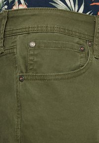 Pantalones verde oliva con una textura suave, que cuentan con costuras en los bolsillos traseros y acentos de metal en los bolsillos.