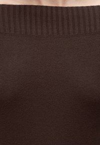 Gros plan d'un vêtement tricoté marron avec un col côtelé, montrant la texture et les détails du tissu.