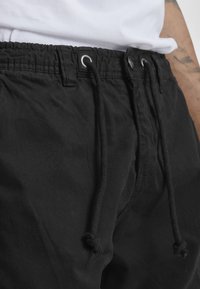 Zwarte drawstring shorts met elastische tailleband, voorzien van metalen oogjes en een gestructureerde stof. De koorden zijn geknoopt voor een veilige pasvorm.