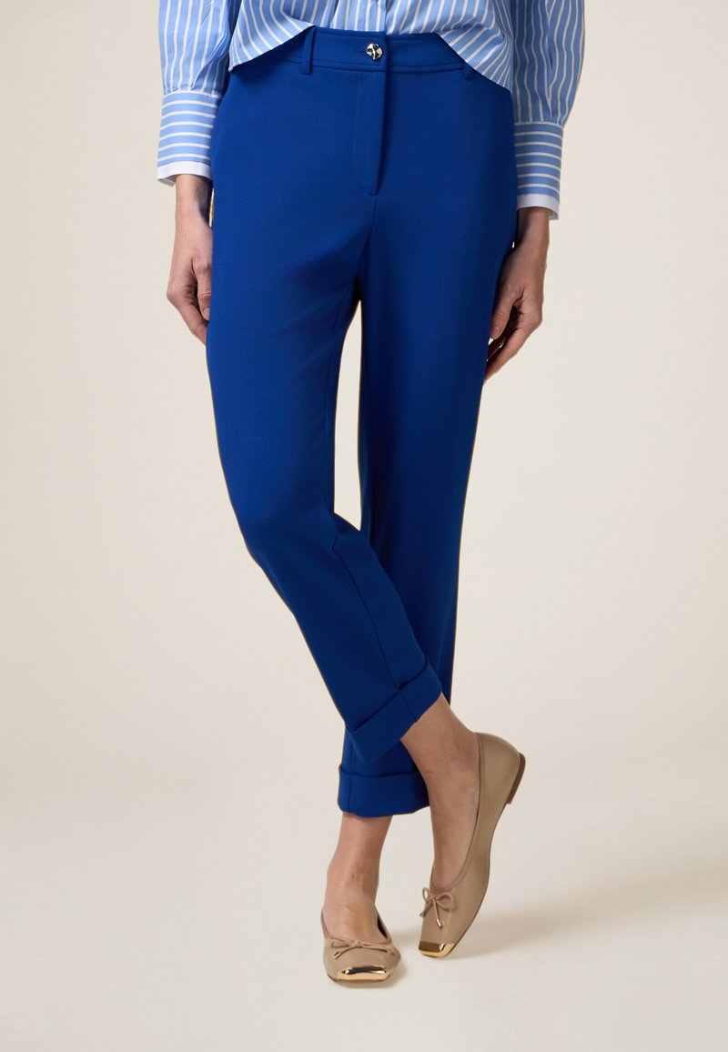 Blauwe op maat gemaakte broeken met opgerolde boorden, voorzien van een flat front en een zilveren knoop. Gecombineerd met beige balletschoenen met gouden accenten.