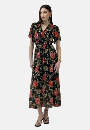 Robe maxi florale noire avec un motif floral rouge et vert, taille smockée, manches courtes et tissu fluide, complétée par des escarpins noirs à lanières.