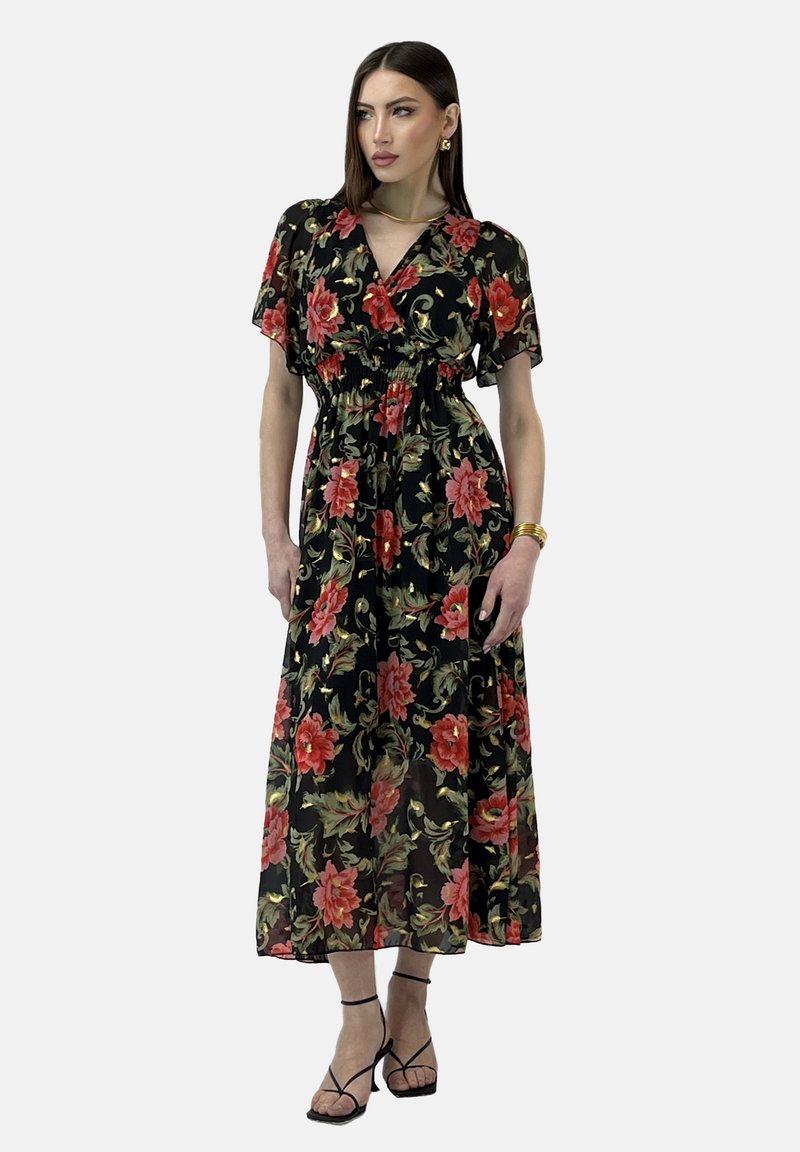 Vestido maxi floral negro con un patrón de flores rojas y verdes, cintura fruncida, mangas cortas y tela fluida, complementado con tacones negros de tiras.