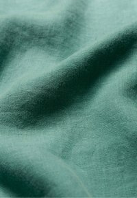 Mīksts zaļas krāsas teksturēts lina audums ar gludu, nedaudz burzītu virsmu un dabīgu, elpojošu kvalitāti.