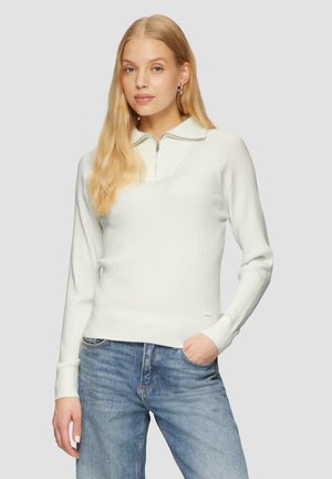 Ribbed white pullover sweater with a quarter-zip neck and a fitted silhouette, paired with light blue jeans. Soft texture and casual design.