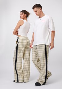 Lys beige rutete bukser med svarte sidestropper, med en vid buksedesign. En tettsittende hvit tanktopp og en oversized hvit T-skjorte er påført.