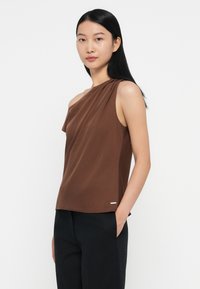 Top marrone senza maniche con design drappeggiato, dotato di una sola spallina. Tessuto morbido, accentuato da un logo minimale vicino all'orlo. Pantaloni neri.