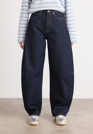 Wide-leg blue denim jeans with a high waist, featuring contrast stitching and front pockets. Paired with a striped long-sleeve shirt.