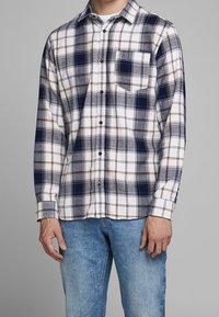 Heren overhemd met lange mouwen in ruitpatroon in marineblauw, wit en bruin. Voorzien van knoopsluiting, een enkele borstzak, zacht katoen en een relaxte pasvorm.