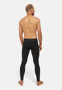 Zwarte sportleggings met een brede elastische tailleband die de merknaam bevat, aansluitende pasvorm, volledige lengte en een gladde textuur.