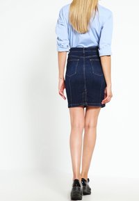 Minifalda de mezclilla en azul oscuro con un corte ajustado, cintura alta, bolsillos traseros y detalles de costura en contraste. Combinada con una camisa azul clara.