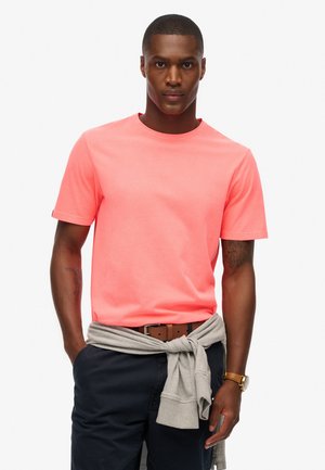 Heldere koraalkleurige katoenen t-shirt met een ronde halslijn en korte mouwen, aangevuld met een grijs sweatshirt dat nonchalant om de taille is geknoopt.