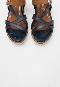 Leder-Sandalen mit dunkelblauen überkreuzten Riemen und einem braunen Knöchelriemen. Strukturiertes Fußbett und hellbeige Sohle.
