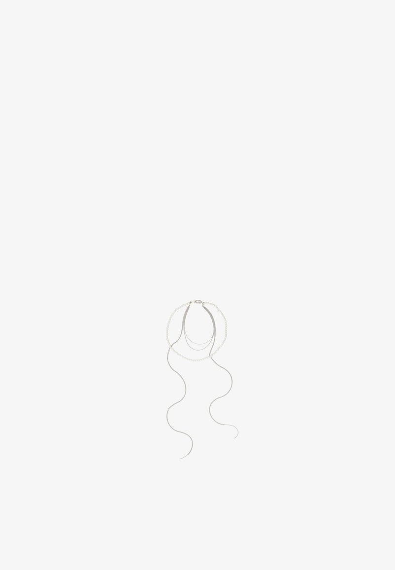 Collier en argent délicat avec des chaînes superposées et de longues fines mèches pendantes sur un fond blanc uni.