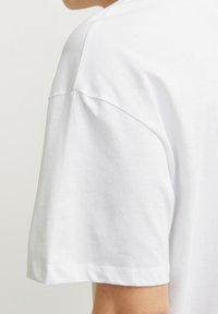 Biała bawełniana koszulka z luźnym krojem, krótkimi rękawami i gładką fakturą. Charakteryzuje się prostym wzorem i minimalnymi detalami przeszyciami.