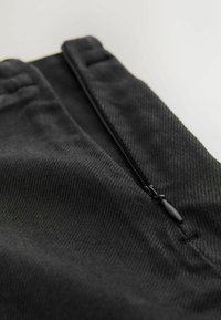 Schwarzer gewebter Stoff mit glatter Textur, mit einem Reißverschluss und flachem Taillenbund. Die Details umfassen eine Naht entlang des Randes.