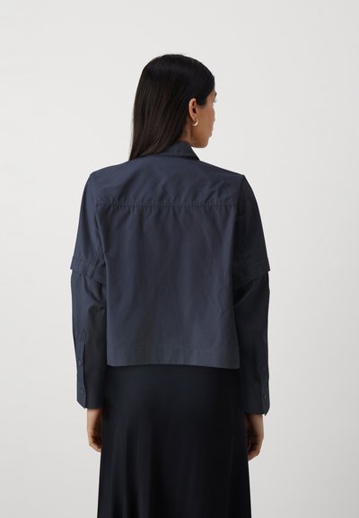 Giubbotto blu navy corto realizzato in tessuto leggero, con colletto classico, polsini con bottoni e una superficie liscia.