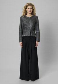 Gray leather jacket with round neck, front buttons, and white stitching. Paired with wide-leg black trousers and a black belt.