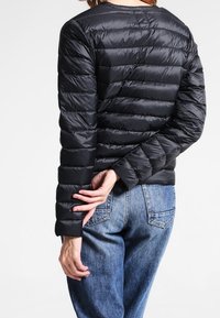 Černá péřová bunda s horizontálním prošíváním, dlouhými rukávy a kulatým výstřihem, doplněná světle modrými džínami.