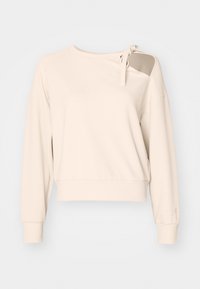 Sudadera beige con un hombro descubierto y detalle de lazo. Presenta mangas largas, puños ajustados y un ajuste relajado. Textura suave.