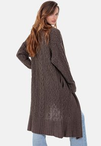 Cardigan long en maille marron avec motifs torsadés texturés, bords côtelés et poches latérales. Fabriqué dans un matériau doux et chaud.