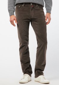 Bruna kordflosbyxor med slim fit, med framfickor, metallknappar och en subtil ribbad textur. Bärs med vita sneakers.