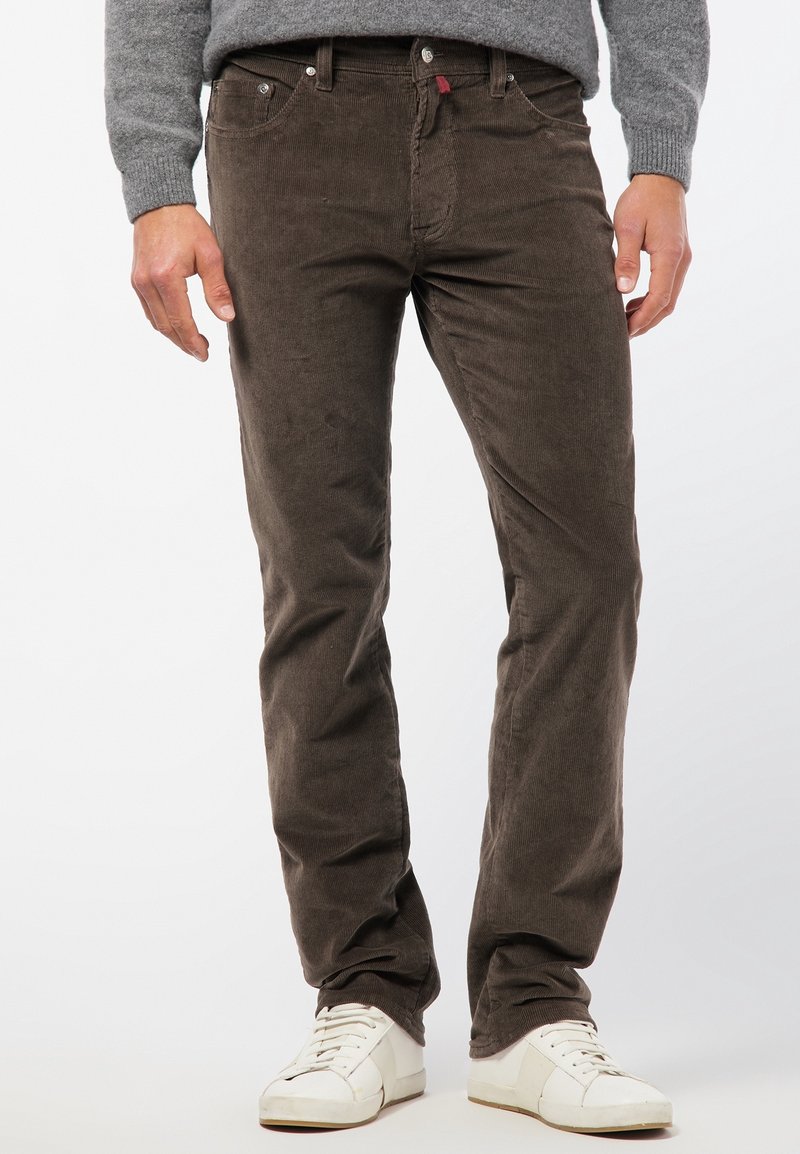 Bruna kordflosbyxor med slim fit, med framfickor, metallknappar och en subtil ribbad textur. Bärs med vita sneakers.