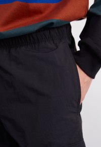 Černé lehké šortky s elastickým pasem a bočními kapsami, doplněné o vícebarevnou pruhovanou mikinu v hnědé, zelené a modré barvě.