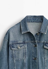 Denim takki vaaleansinisessä pesussa, jossa on klassinen kaulus, kaksi rintataskua ja metallinapit. Kankaassa on tekstuuria.