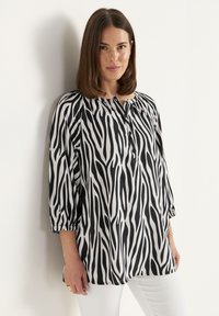 Zwart-witte blouse met zebraprint, ronde halslijn, driekwart mouwen en knoopdetail aan de voorkant. Zijdezachte textuur, losse pasvorm.