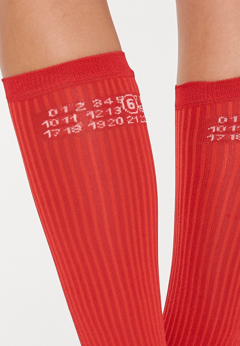Red knee-high socks with a ribbed texture, soft material, and white printed numbers arranged in a grid pattern near the top.
