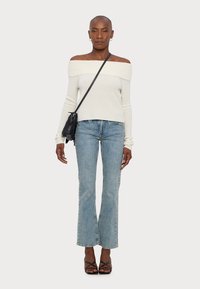 Turtlenek kakovosti iz bež barve z odprtimi rameni, svetlo modri flared jeans, črne sandale s križnim trakovi in majhna črna torbica s fricami.