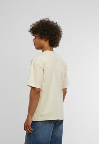 Beige kortermet t-skjorte laget av bomull, med rund hals og avslappet passform. Bakvisning med lett tekstur og uten synlige grafikker.