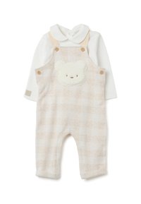 Canzoniere a scacchi beige per bambini con una morbida patch a forma di orsetto sul davanti, dotato di bottoni in legno e una maglietta bianca a maniche lunghe sotto.