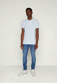 Polo azul claro com colarinho, combinado com jeans azuis ajustados e sapatilhas brancas. Design simples com detalhes mínimos e textura suave.