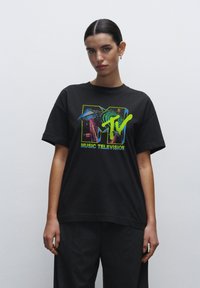 Sort bomulds T-shirt med et farverigt MTV grafik med et rumskib og svulstige mønstre. Korte ærmer, rund halsudskæring, afslappet pasform.