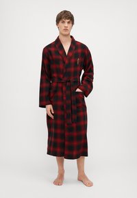 Raudonas ir juodas languotas chalatas su šaliku, iki kelių ilgio, ilgomis rankovėmis, su maža logotipo etikete ant krūtinės ir kišene vienoje pusėje.