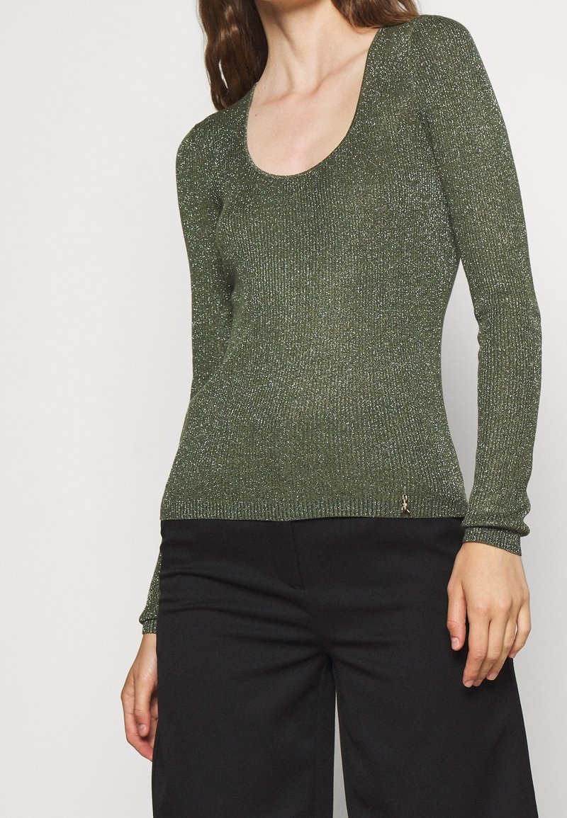 Haut à manches longues côtelé vert olive avec un col rond et une texture scintillante. Coupe slim, avec un petit détail de marque sur l'ourlet.