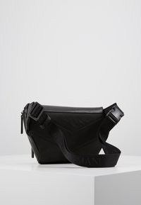 Černá krosbody taška s kombinací texturované kůže a hladké látky, nastavitelného popruhu s logem a zipovým uzávěrem.