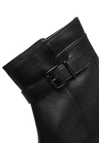 Bottine en cuir noir avec une texture lisse, dotée d'une boucle en haut et de coutures visibles le long de la couture.
